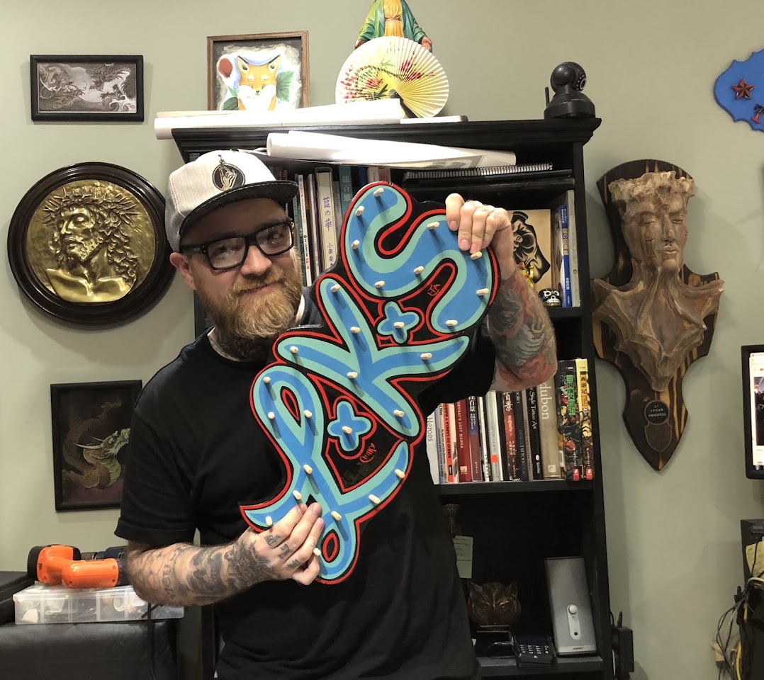 Tatuador de LKS Tattoo con el cartel del estudio